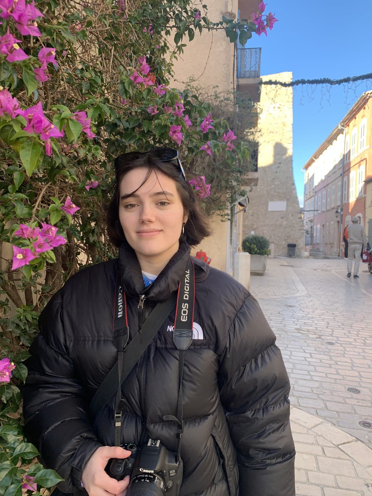 Ester Girona Pascual with her camera, under bougainvillea on a sunny street