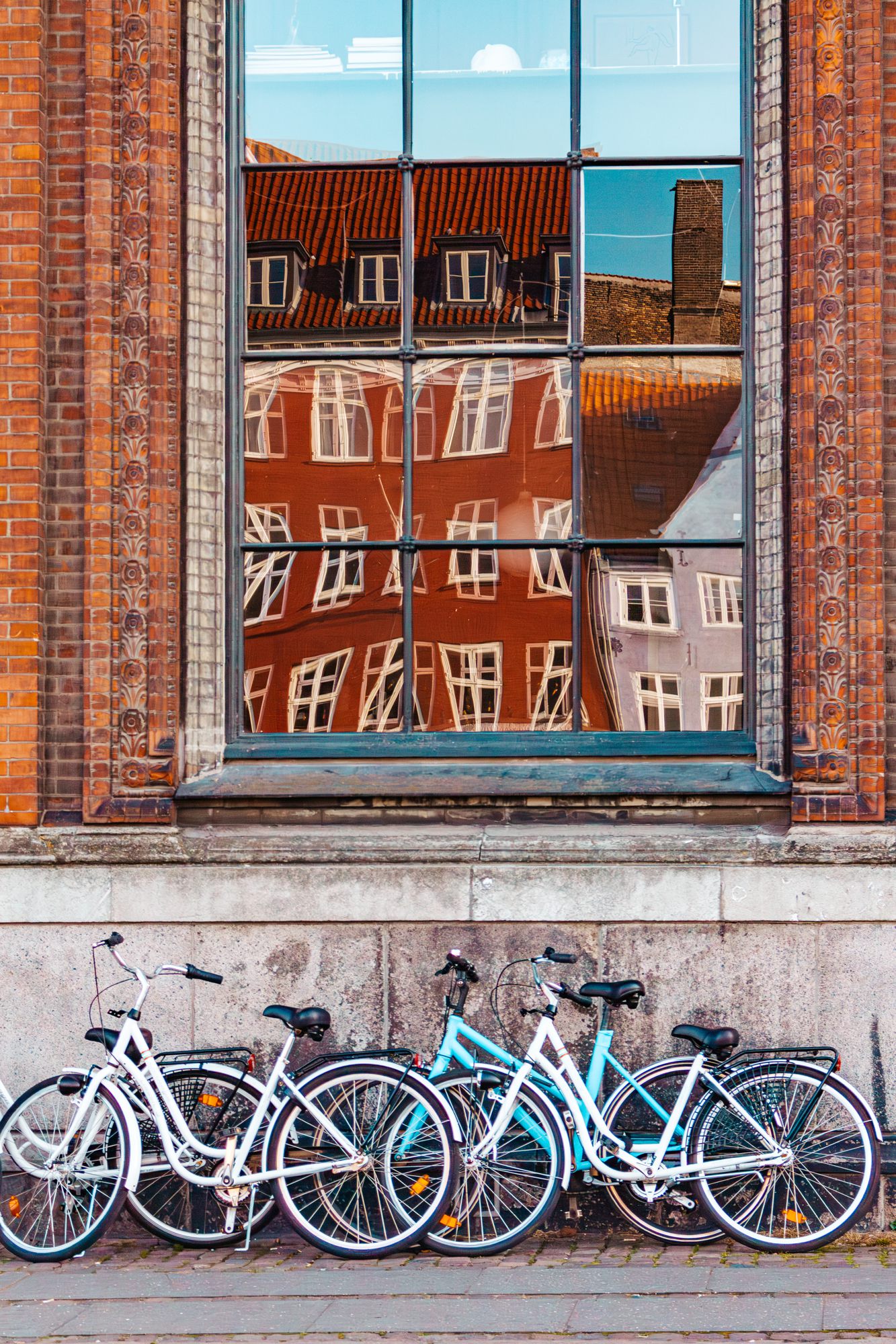 Bicycles parked under a window reflecting brick buildings